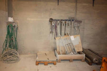 Various lifting chains + buckle straps and more on wall including adapter + pallet with rubber rollers + pallet with miscellaneous + pallet with cardboard + air hoses on the wall