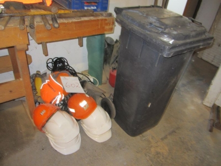 Grå affaldscontainer, sikkerhedshjelme, kabler, støvler mm på gulv
