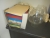 Indpakningspapir, 2 glasbovle, kasse farvet karton i forskellige farver mm på bord