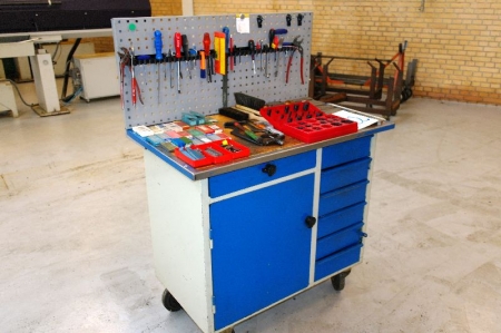 Workshop table on wheels with shelves and drawers and tool panel containing various hand tools, gaskets, etc.