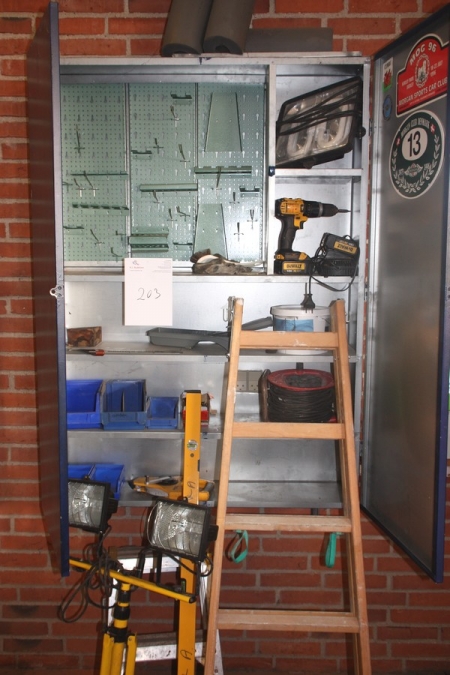 Tool cabinet on the wall with content: cordless drill, DeWalt with 2 batteries and charger + work lamps, tape, cable drum, wooden stepladder, etc.